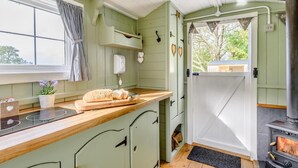 Et køkken med træbordplade, et brød, et vindue med gardiner, en hvid dør og en brændeovn.