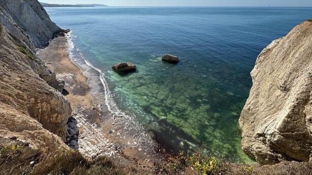 Un paisaje costero con acantilados, agua cristalina y dos rocas destacadas.