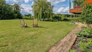 Una casa moderna con un jardín amplio, dos sillas de jardín y un árbol.