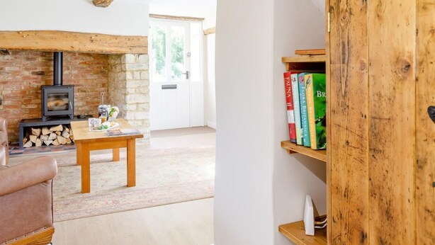 Una sala de estar acogedora con vigas de madera a la vista, una chimenea de piedra, una mesa de madera y una estantería.