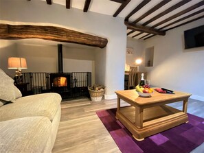 A living room with a sofa, a wooden table with fruit, a fireplace, and a lamp. - 4 Bed in Llanrwst (oc-66510) (Llanrwst)