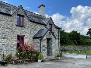 A stone building with red-framed windows, a chimney, and a small porch area with potted plants. - 4 Bed in Llanrwst (oc-66510) (Llanrwst)
