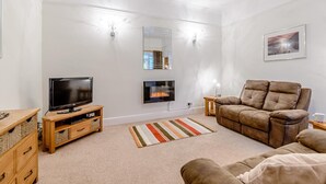 Una sala de estar con televisión de pantalla plana, chimenea, sofá, aparador de madera y alfombra a rayas.