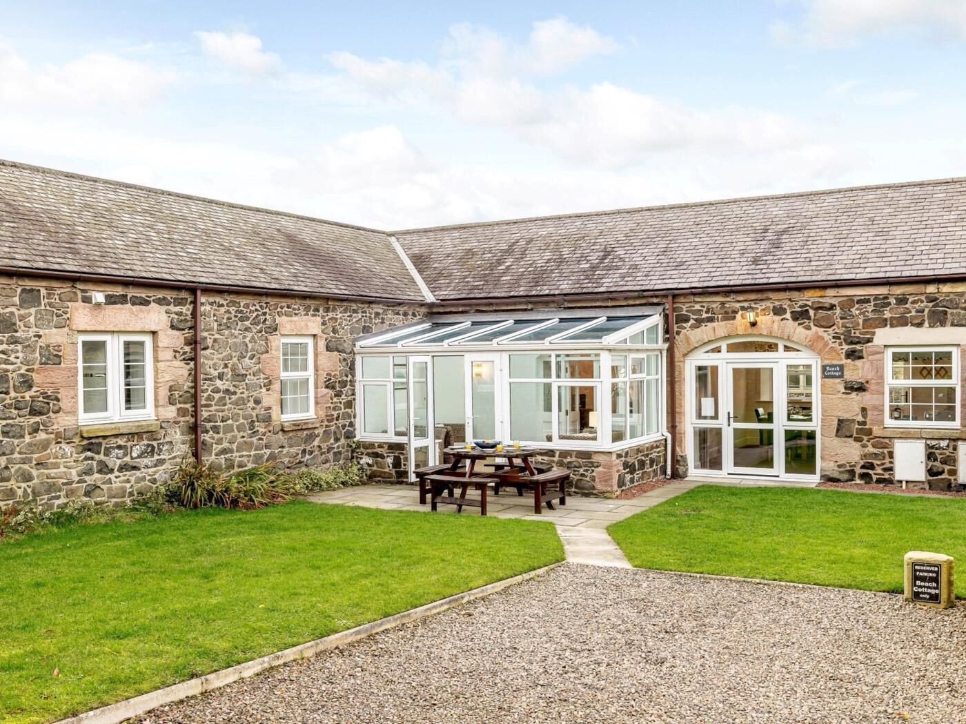 A stone building with a conservatory, a patio table, and a gravel path.