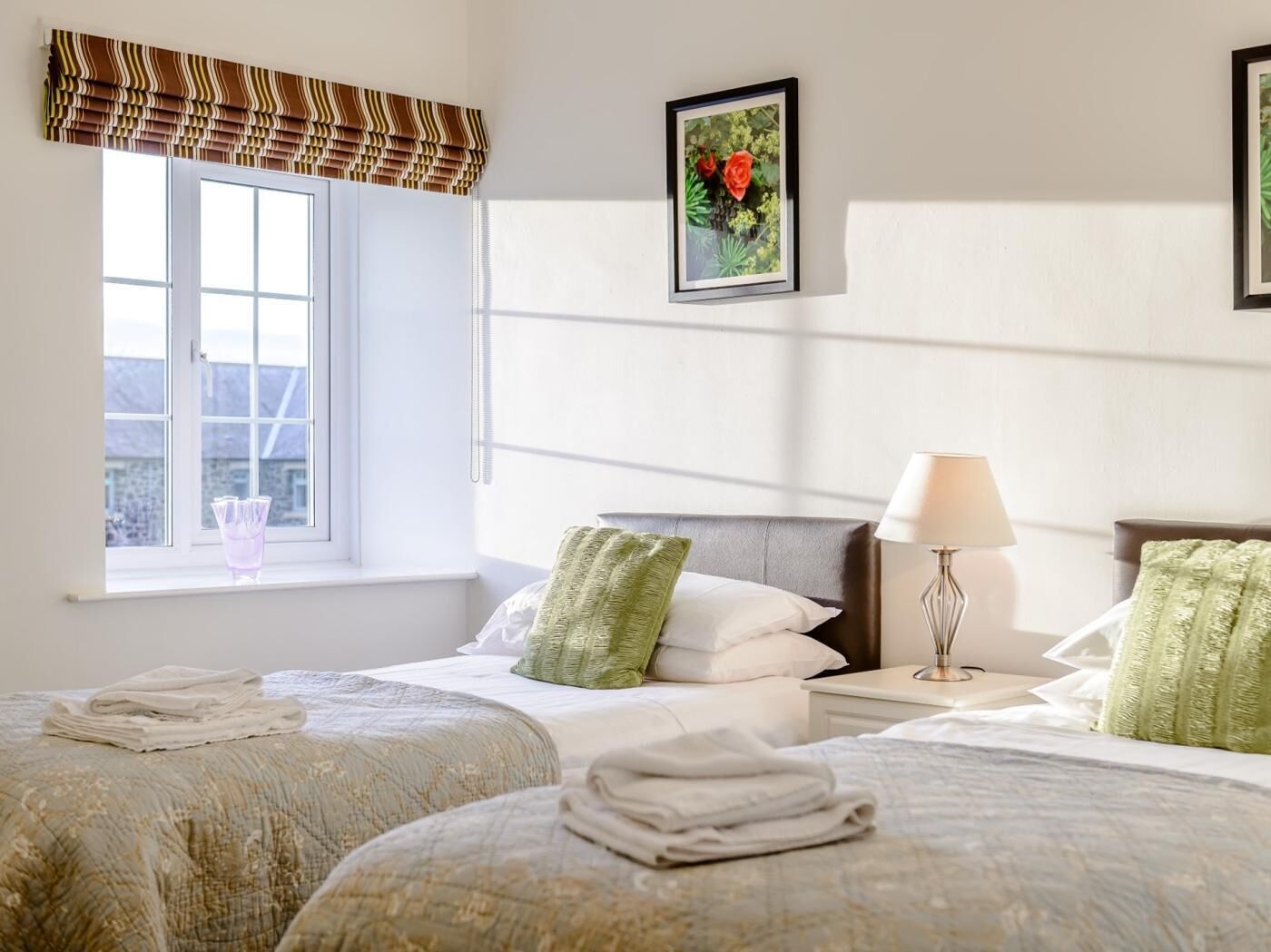 Une chambre d’hôtel avec deux lits, une fenêtre donnant sur un beau paysage, un tableau encadré au mur et une lampe de chevet.