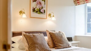 Habitación de hotel con una cama, dos lámparas de pared, un cuadro con flores y un ventanal con cortinas.