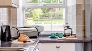 Una cocina con un tostador, un hervidor, una hogaza de pan y una cafetera sobre la encimera.