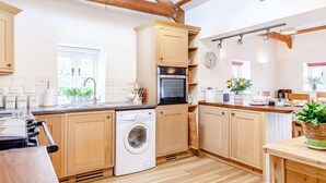 A kitchen with wooden cabinets, a washing machine, a stove, and a sink. - 2 Bed in St. Austell (oc-79594) (Coombe)
