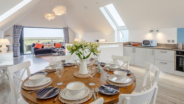 A dining area with a round table set for four, a kitchen with modern appliances, and a living area with a view. - 4 Bed in Bideford (oc-72587) (Northam)