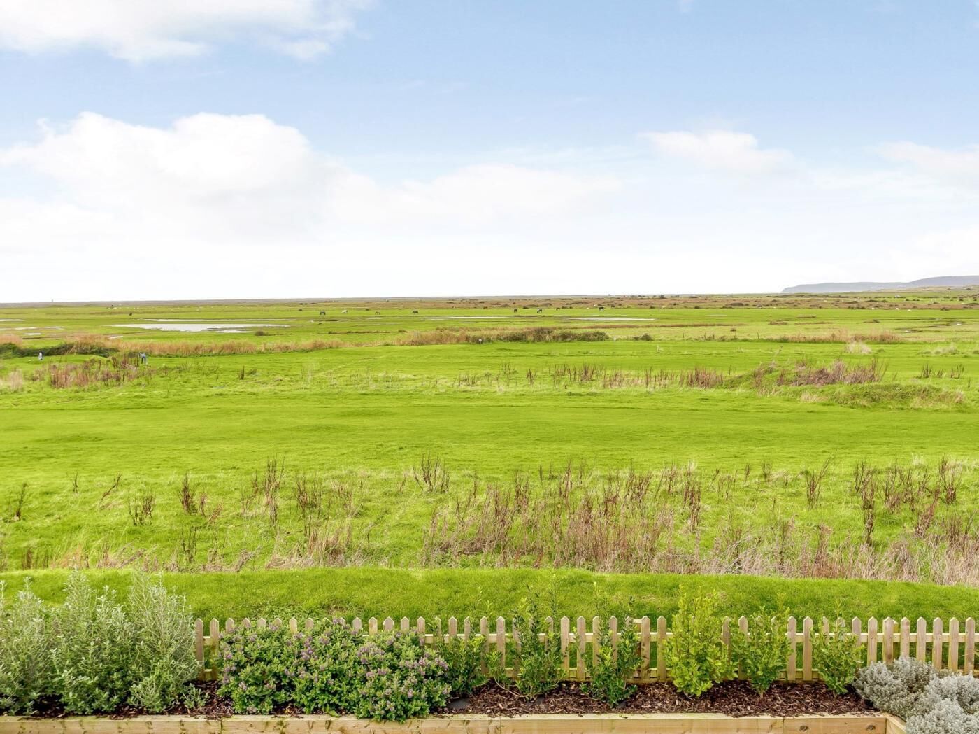 A vast green field with a wooden fence in the foreground.