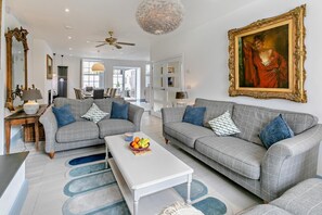 Ein geräumiges Wohnzimmer mit zwei grauen Sofas, einem weißen Couchtisch und einem großen Gemälde an der Wand.