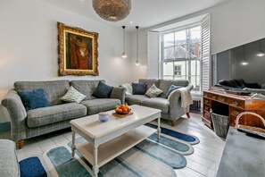Ein modernes Wohnzimmer mit zwei grauen Sofas, einem weißen Couchtisch, einem Gemälde an der Wand und einem großen Fenster.