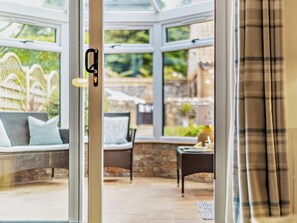 A conservatory with a glass door, wicker furniture, and a stone wall in the background. - 3 Bed in Sheringham (oc-ncc77) (Upper Sheringham)