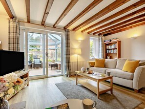 A living room with a television, sofa, coffee table, and a bookshelf. - 3 Bed in Sheringham (oc-ncc77) (Upper Sheringham)