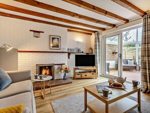 A living room with a fireplace, a television, a sofa, a coffee table, and a view of the outdoors. - 3 Bed in Sheringham (oc-ncc77) (Upper Sheringham)