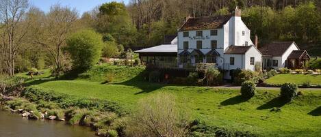 A white building with a sign 'The Woodbridge Inn' in a rural setting with a river and greenery.