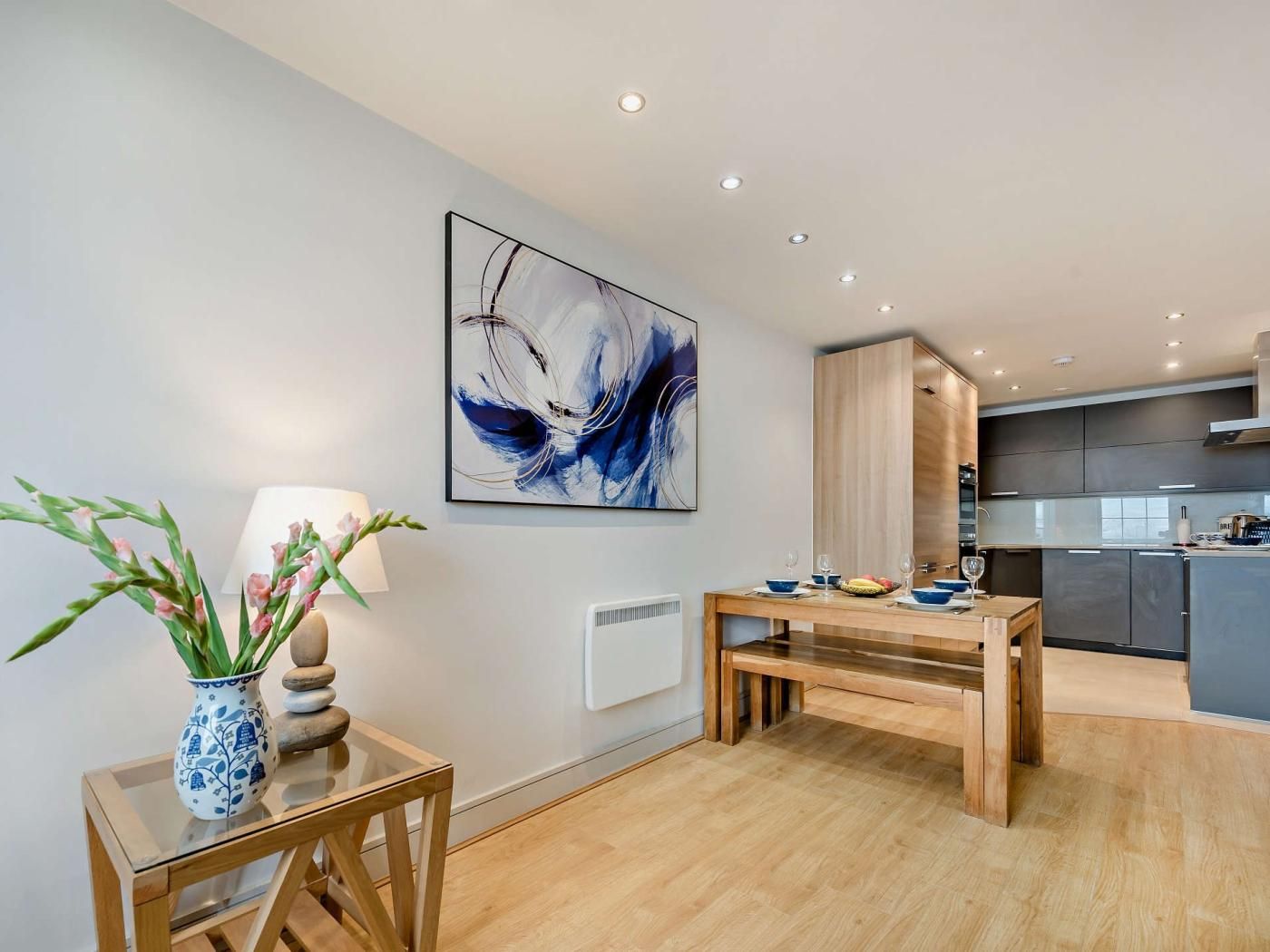 A modern kitchen with built-in appliances, a dining area with a wooden table and chairs, and a wall-mounted abstract painting.