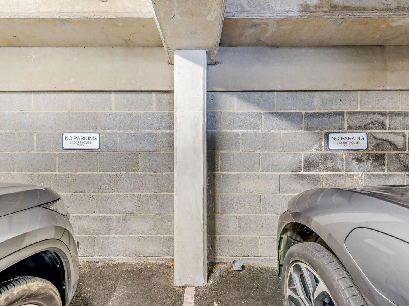 Een parkeerplaats met twee auto's, een bakstenen muur en twee borden met de tekst 'GEEN PARKEREN 9 COURT HOUSE ALLEEN'.