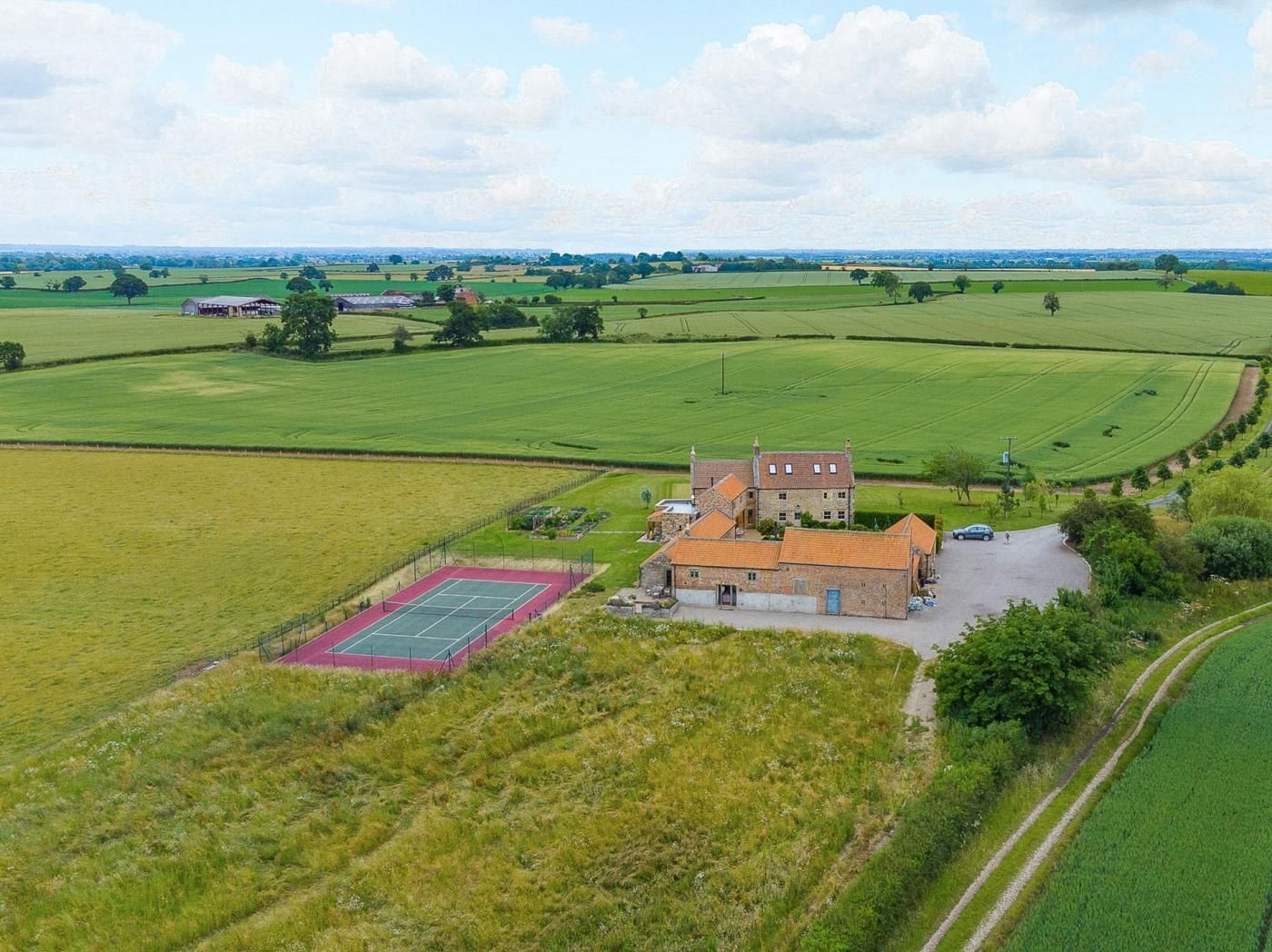 Een landelijk gelegen bezit met een groot huis, een tennisbaan en uitgestrekte groene velden.