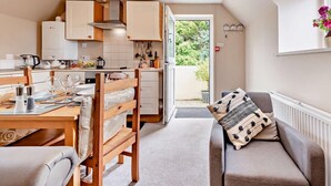 A modern kitchen with white cabinets, a dining area with a wooden table and chairs, and a view of the outdoors through a glass door. - 2 Bed in Cosheston (oc-fb059) (Cosheston)