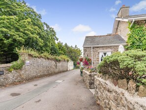 A narrow street with stone walls, a stone building with a white door, and a garden with colorful flowers. - 2 Bed in Cosheston (oc-fb060) (Cosheston)