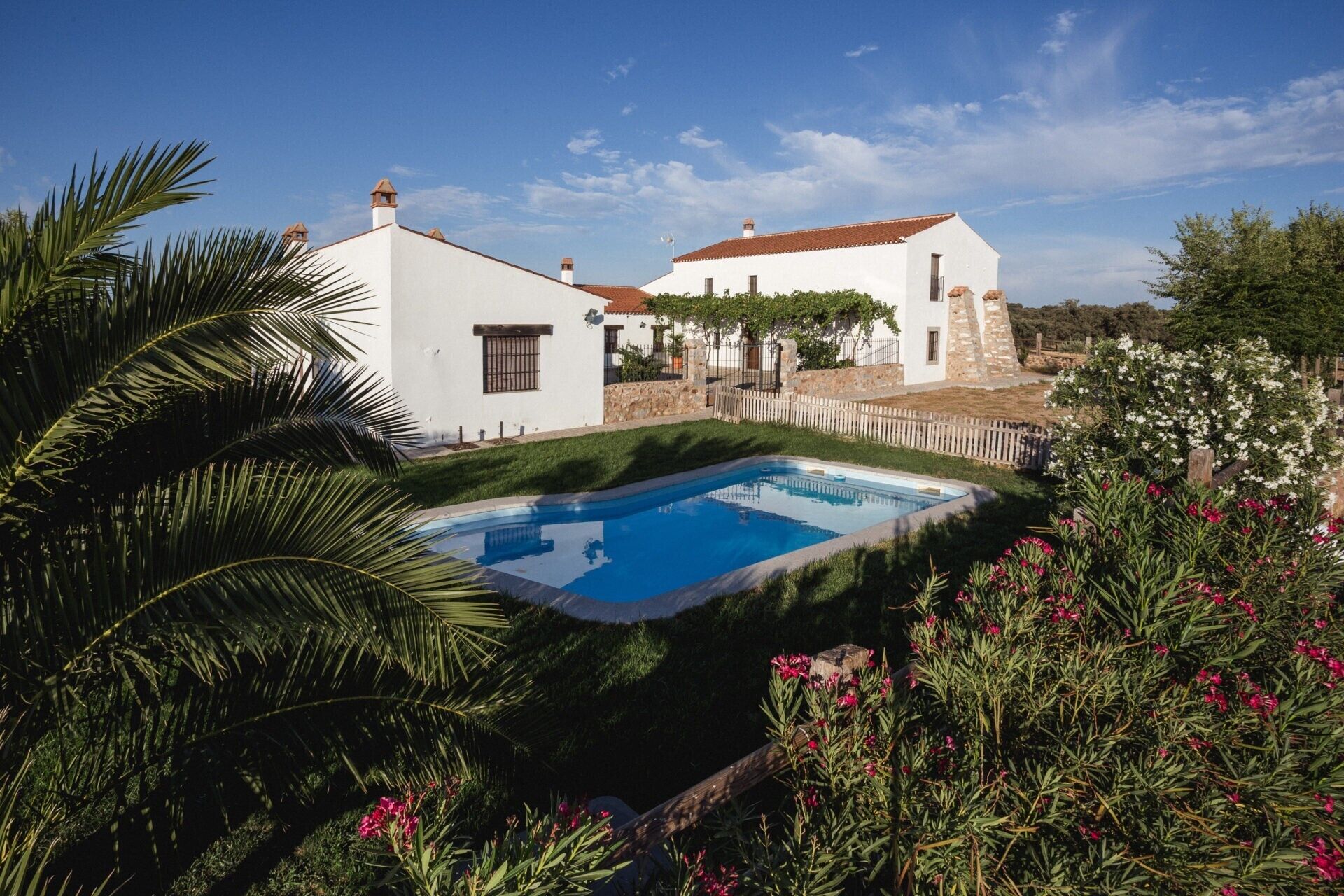 Una villa blanca con piscina, rodeada de follaje y flores.