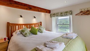 Une chambre à coucher avec une tête de lit en bois, une grande fenêtre donnant sur un beau paysage, une table de chevet et un lit avec des oreillers et des serviettes.
