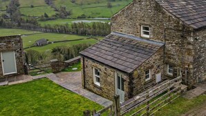 Un bâtiment en pierre avec un toit en pente, une petite construction attenante et une vue sur des champs verdoyants.