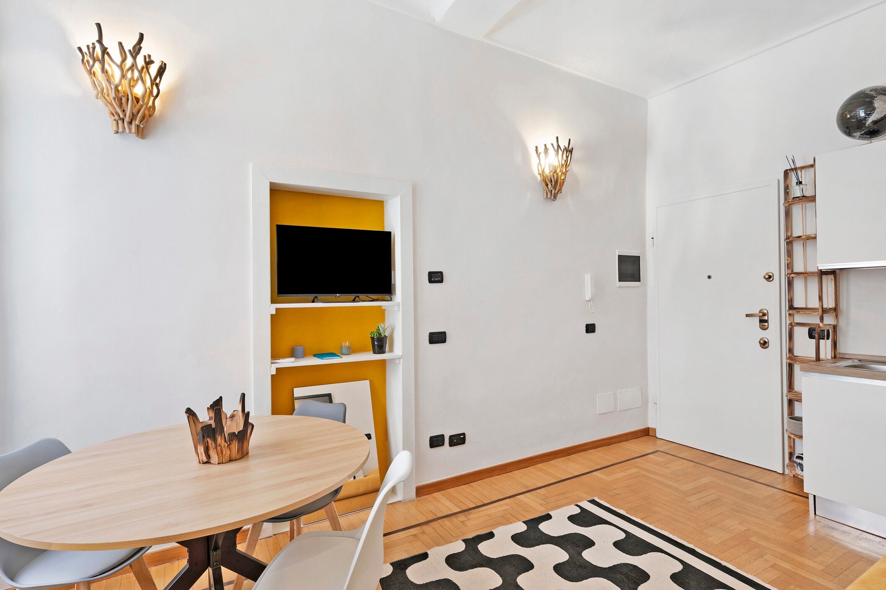 Un interior moderno con una mesa redonda de madera, sillas blancas, una pared de acento amarilla y estanterías empotradas.