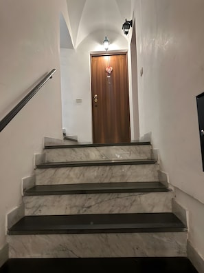 Un escalier en marbre mène à une porte en bois surmontée d’un luminaire.
