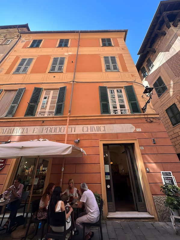 Un bâtiment sur lequel on peut lire l’inscription « Farmacia E Prodotti Chimici », et un groupe de personnes assises à une table à l’extérieur.