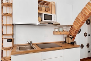 A kitchen with a built-in microwave, a sink, and a wooden shelf with jars. - Casa Marchesi – Cozy Apartment with Wi-Fi and Air Conditioning (Albenga)