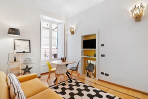 Una sala de estar moderna con un sofá, una mesa de comedor redonda, sillas, una decoración en forma de estrella, una lámpara, un televisor y una lámpara de pared.