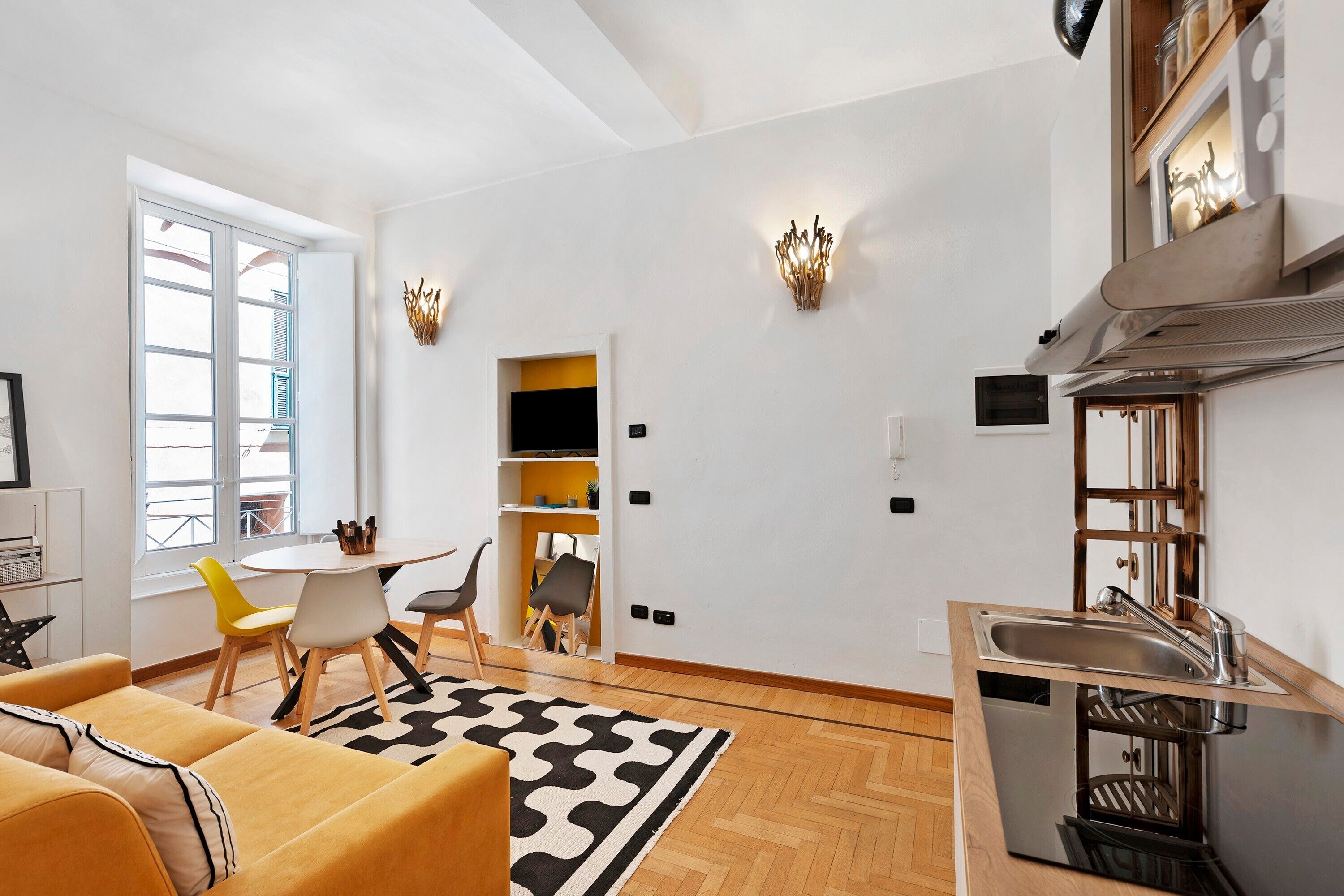 Una cucina moderna con piano cottura integrato, un'area pranzo con tavolo e sedie rotonde, e un piccolo angolo salotto con divano.