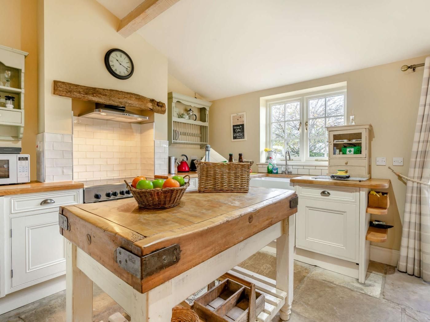 A kitchen with a wooden island, white cabinetry, a clock on the wall, and a window with a view.