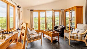 A spacious living area with a chessboard, wooden furniture, and large windows offering a view of the countryside. - 4 Bed in Brecon (oc-82529) (Crai)
