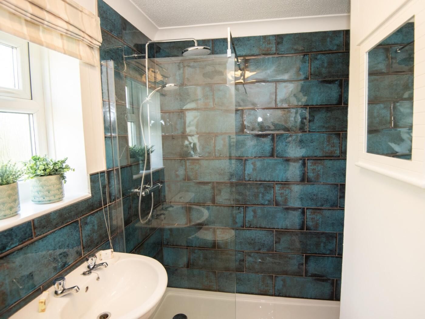 Une salle de bain avec une douche à parois de verre, un lavabo blanc et un mur recouvert de carreaux.