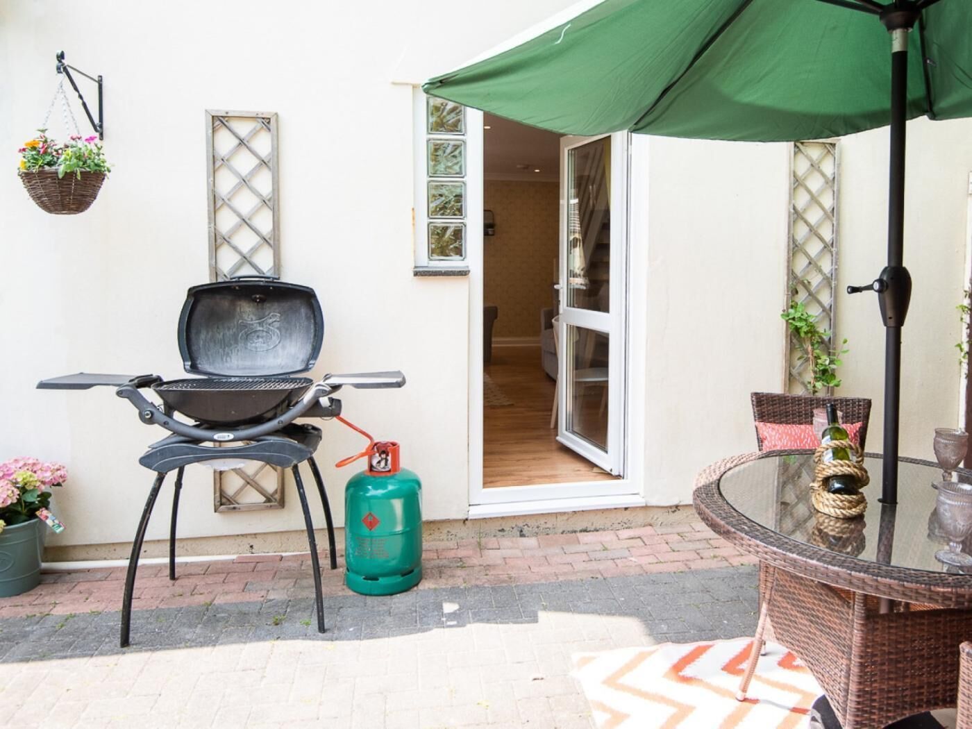 Un patio con una parrilla, una mesa de vidrio y un paraguas verde.