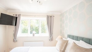 Une chambre à coucher avec un lit, un téléviseur fixé au mur, une fenêtre avec des rideaux et un radiateur.