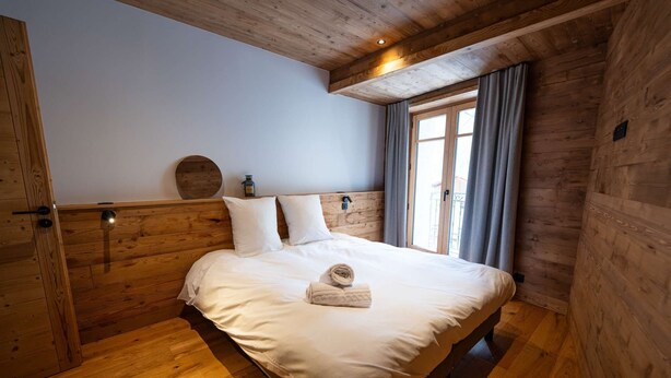 Une chambre aux murs lambrés, avec un lit, des oreillers et une fenêtre ornée de rideaux.