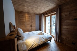 Ein Schlafzimmer mit Holzboden, Bett mit weißer Bettwäsche, einem Fenster mit Vorhängen und einer Holzbalkendecke.