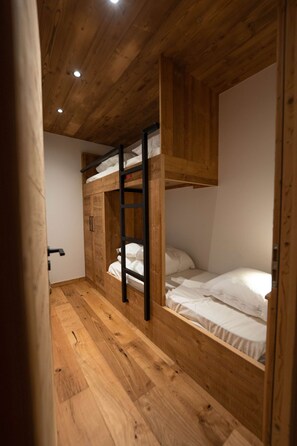 Une chambre avec un lit superposé en bois, une échelle, une armoire et une porte.