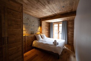 Ein Schlafzimmer in einer Holzhütte mit einer Steinwand, einem Bett mit weißer Bettwäsche und einem Fenster mit Vorhängen.