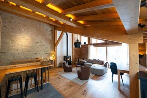 Un intérieur rustique avec des poutres apparentes, un mur en pierre, une cheminée et un coin salon confortable.