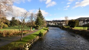 Ein Fluss mit einer Steinmauer und einer Brücke, umgeben von Grünflächen und Gebäuden.