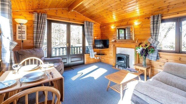 Ein Holzblockhaus-Interieur mit einer Couch, einem Esstisch, einem Fernseher, einem Kamin und großen Fenstern.