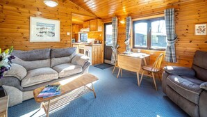 Ein gemütliches Blockhauss-Interieur mit einer Couch, einem kleinen Esstisch und einer Küchenzeile.