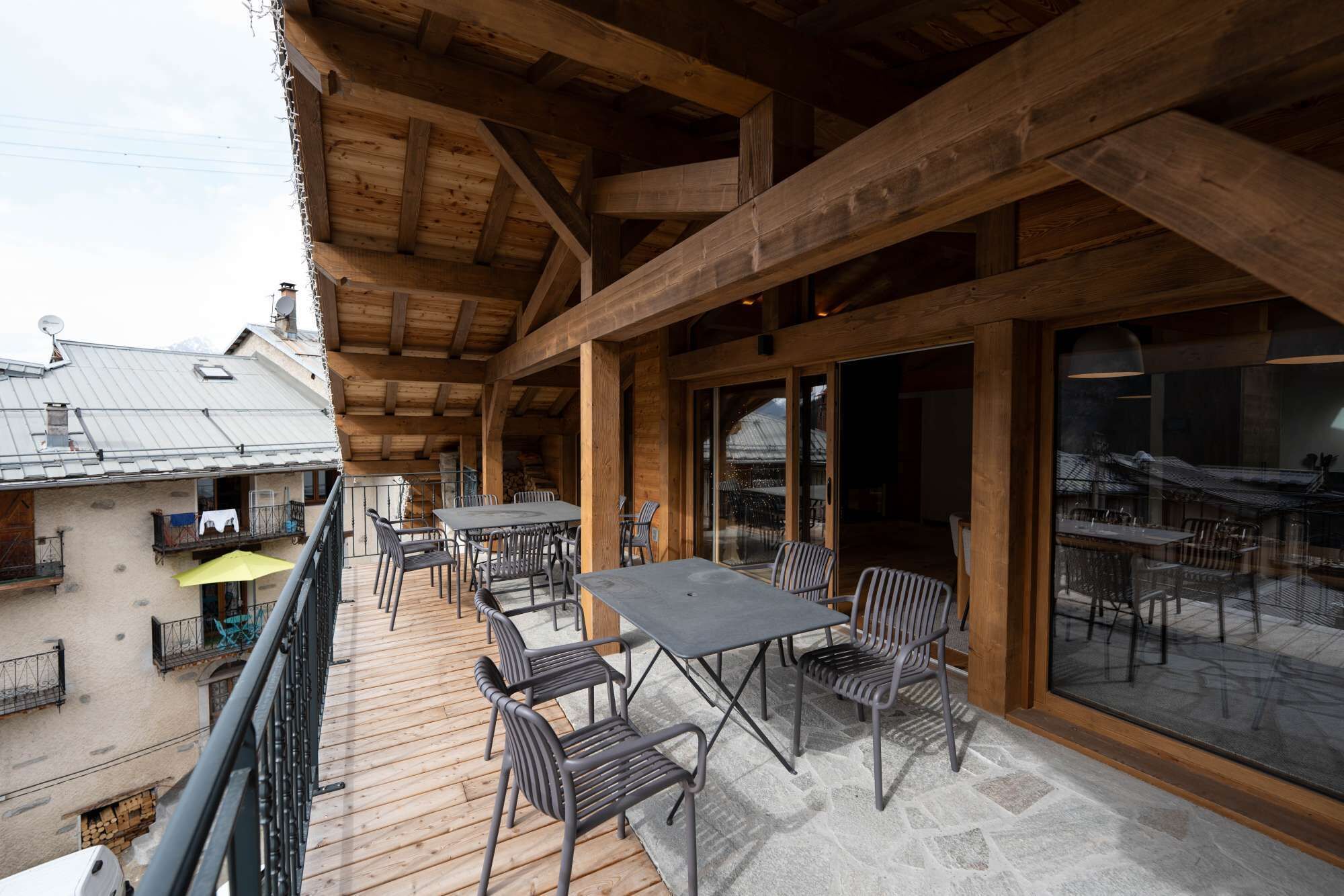 A wooden deck with outdoor seating, a balcony, and large windows.