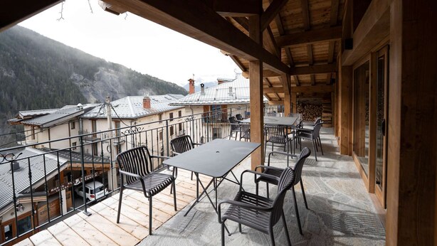 Een houten balkon met tafels en stoelen, met uitzicht op een bergachtig landschap.