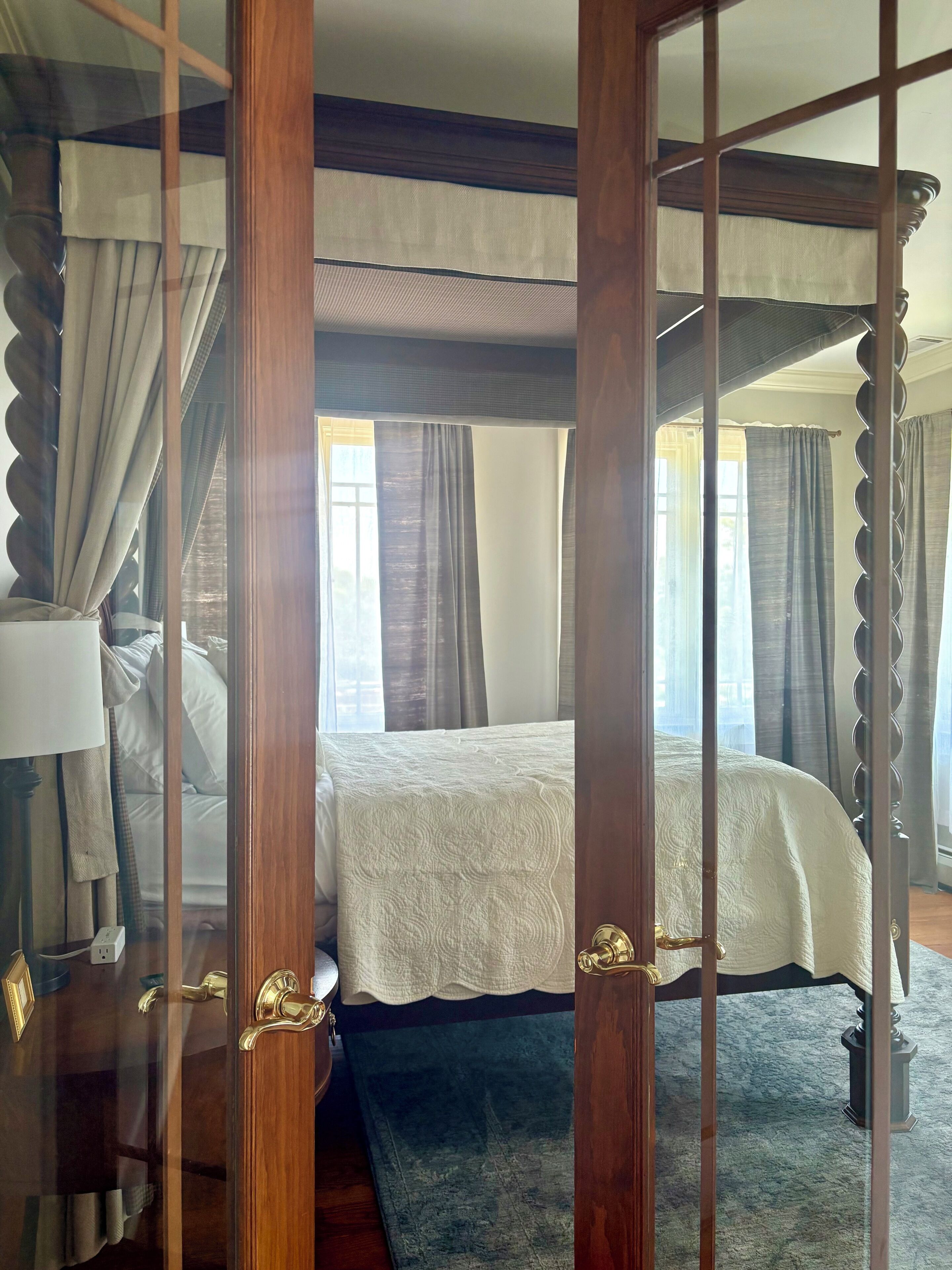 A four-poster bed with a white bedspread, a wooden floor, and a blue rug.